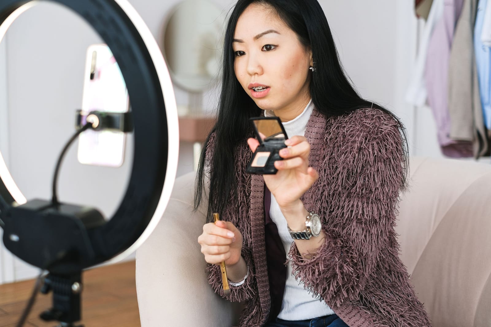 Mulher mostra uma paleta de sombras para o celular preso no ring light enquanto grava um vídeo de maquiagem