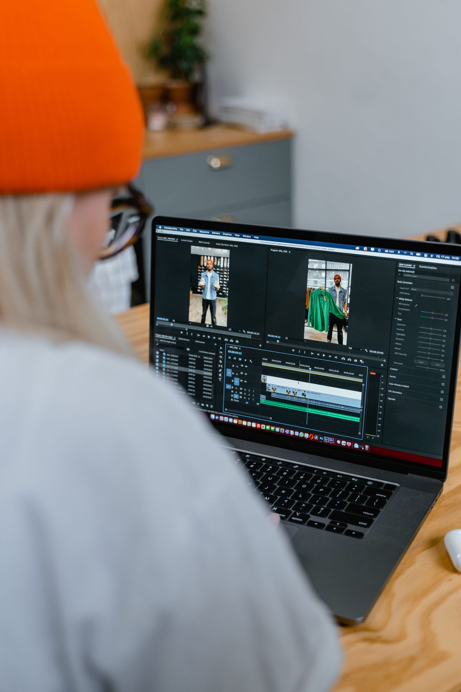 Mulher de gorro laranja edita no notebook um vídeo vertical de moda, com a linha do tempo da edição na tela
